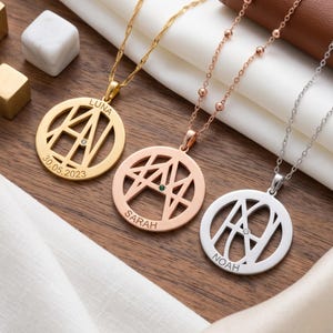 Könnte beinhalten: Drei runde Kettenanhänger in Gold-, Roségold- und Silbertönen. Jeder Anhänger verfügt über einen stilisierten Monogramm-Ausschnitt, einen kleinen eingebetteten Edelstein und eingravierte Namen wie Luna, Sarah und Noah, mit einem Datum auf dem goldenen Stück.