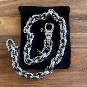 May include: A heavy silver-toned metal chain featuring large, thick oval links. The chain includes a prominent lobster claw clasp with an engraved star and crown emblem, along with a screw-lock shackle connector at the opposite end of the chain.