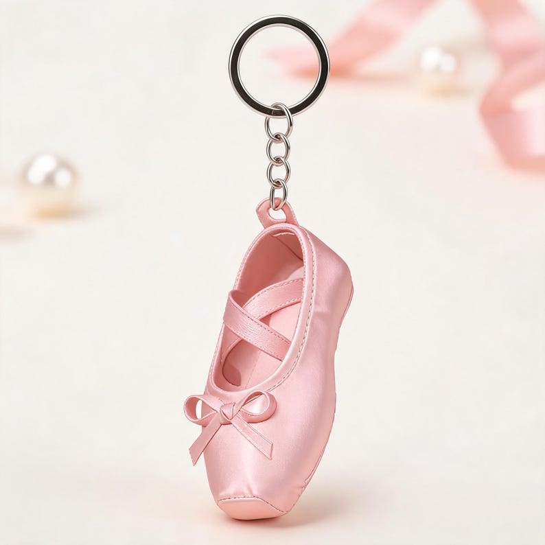Puede incluir: Un llavero de zapatilla de ballet rosa claro con un acabado satinado suave, tiras el&aacute;sticas cruzadas en la parte superior y un peque&ntilde;o lazo decorativo en la punta. El zapato est&aacute; unido a una anilla de metal plateado mediante una cadena.