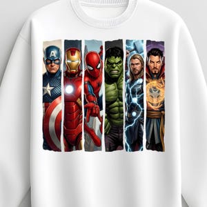 May include: White sweatshirt featuring a colorful graphic of several superheroes, including Captain America, Iron Man, Spider-Man, Hulk, Thor, and Doctor Strange. The design showcases the characters in a vertical, segmented arrangement.