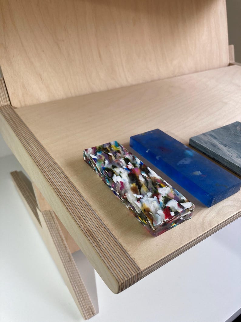 May include: A wooden desk with a light finish, featuring rectangular blocks of various colors and textures. One block is a mix of colors, another is blue, and a third is gray. The desk has a simple, modern design.