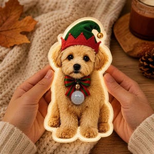 May include: A light-up cutout of a fluffy golden puppy wearing a green and red elf hat with a small gold bell. The puppy has a red and green striped bow tie with a central gold bell and a circular motion sensor light attached to its chest.