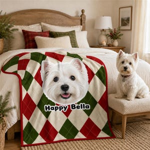 Op de afbeelding: Een zachte plaid met een ruitpatroon in rood, groen en crème. In het midden van de deken staat een groot, gedetailleerd portret van een witte West Highland White Terrier met de tekst Happy Bella in het zwart eronder gedrukt.