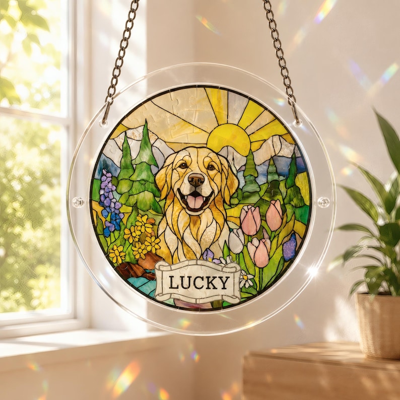 Round acrylic puzzle suncatcher hanging by a stainless steel chain in front of a sunny window, featuring a happy golden retriever surrounded by colorful flowers and green trees, with a yellow sun rising in the background. The suncatcher has a clear border and a nameplate at the bottom reading ‘LUCKY,’ with soft rainbow light reflections on the wall and windowsill nearby.