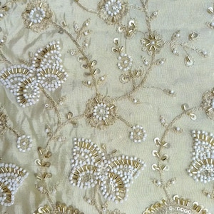 Könnte beinhalten: Ein hell champagnerfarbener Stoff mit aufwendigen Stickereien von Blumen und Schmetterlingen. Das Design ist mit kleinen weißen Perlen, goldfarbenen metallischen Stiftperlen und flachen goldenen Pailletten in Blumen- und Insektenmustern verziert.