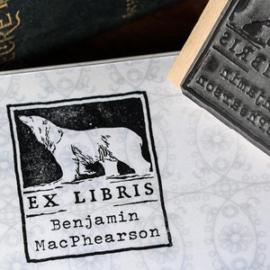 Peut inclure: Un tampon en bois pour livre avec un motif en caoutchouc noir représentant un ours polaire et le texte "Ex Libris Benjamin MacPhearson".