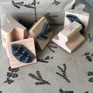 May include: A set of five wooden stamps with a sprig of pine design. The stamps are on a brown paper background with a printed pine sprig design. The stamps are labeled "The English Stamp Company".