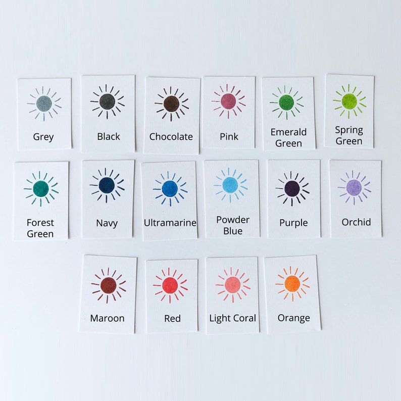 May include: A collection of color swatches arranged on a white surface. Each swatch is a small white rectangle with a sunburst design and a color name printed below. Colors include grey, black, chocolate, pink, emerald green, and spring green.