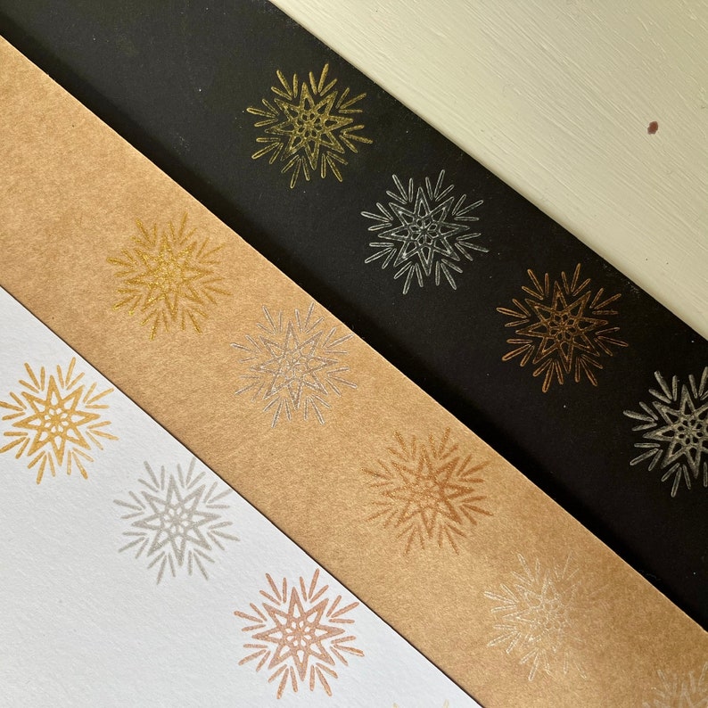 May include: Three strips of paper with different colored star designs. The top strip is black with gold stars, the middle strip is brown with silver stars, and the bottom strip is white with copper stars.