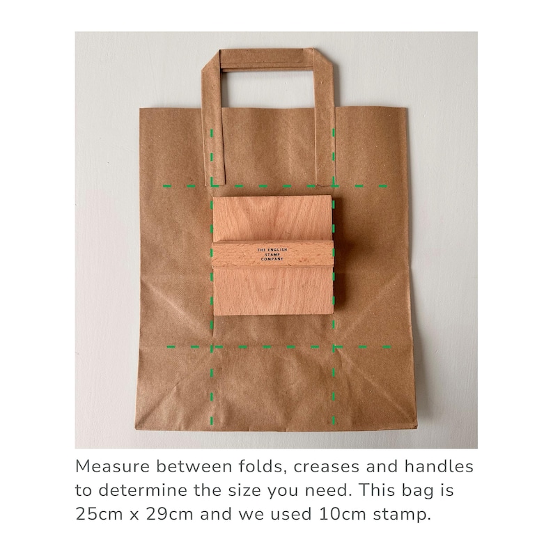 K&ouml;nnte beinhalten: Eine braune Papiert&uuml;te mit einem Muster aus gr&uuml;nen gestrichelten Linien. Die Tasche ist gefaltet, um die Gr&ouml;&szlig;e eines 10 cm gro&szlig;en quadratischen Stempels zu zeigen. Der Stempel ist aus Holz und tr&auml;gt den Text "THE ENGLISH STAMP COMPANY". Messen Sie zwischen den Falten, Knickfalten und Griffen, um die ben&ouml;tigte Gr&ouml;&szlig;e zu ermitteln. Diese Tasche ist 25 cm x 29 cm gro&szlig; und wir haben einen 10 cm gro&szlig;en Stempel verwendet.