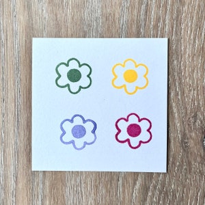 May include: Four simple flower stamps in different colours: green, yellow, purple, and red. Each stamp has a circle in the centre.