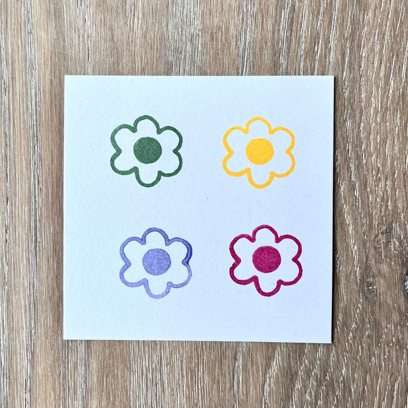 May include: Four simple flower stamps in different colours: green, yellow, purple, and red. Each stamp has a circle in the centre.