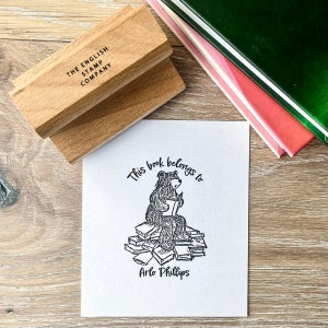 Peut inclure: Une illustration en noir et blanc d'un ours assis sur une pile de livres. L'ours tient un livre dans ses pattes et lit. Le texte "This book belongs to Arlo Phillips" est imprimé sous l'illustration.