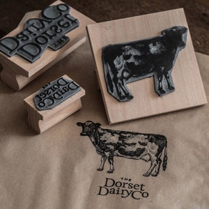 May include: Three wooden blocks with black ink stamps of a cow and the text "The Dorset Dairy Co."