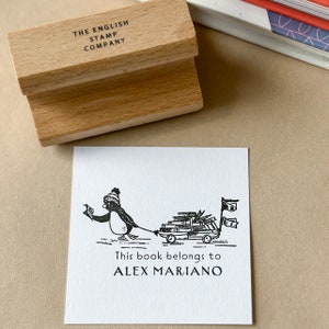 Può includere: Un timbro in gomma nero e bianco con un pinguino che tira un carrello pieno di libri. Il timbro recita "This book belongs to ALEX MARIANO" e "THE ENGLISH STAMP COMPANY".