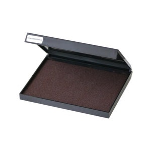 Puede incluir: Una almohadilla de tinta negra con una almohadilla de tinta marr&oacute;n en su interior. La etiqueta en la almohadilla de tinta dice "Chocolate Brown".