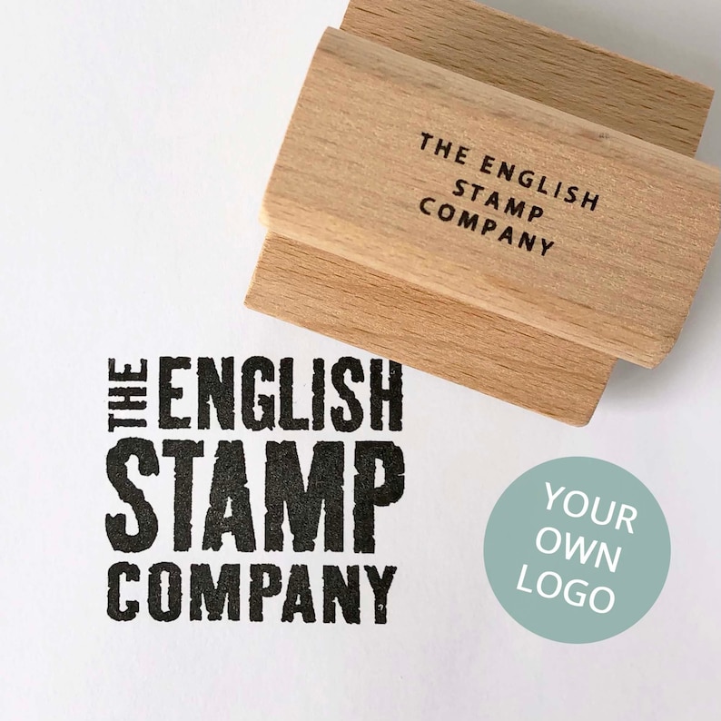 May include: A wooden stamp with the text "THE ENGLISH STAMP COMPANY" on the top and "THE ENGLISH STAMP COMPANY" in a bold, black font on the bottom. A light blue circle with the text "YOUR OWN LOGO" is to the right of the stamp.