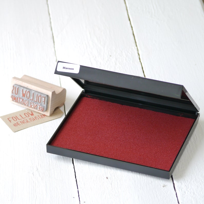 May include: A maroon ink pad in a black plastic case. The ink pad is open and the ink is visible. The ink pad is labeled "Maroon".