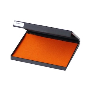 May include: An open orange ink pad in a black plastic case. The label on the case reads "Orange".