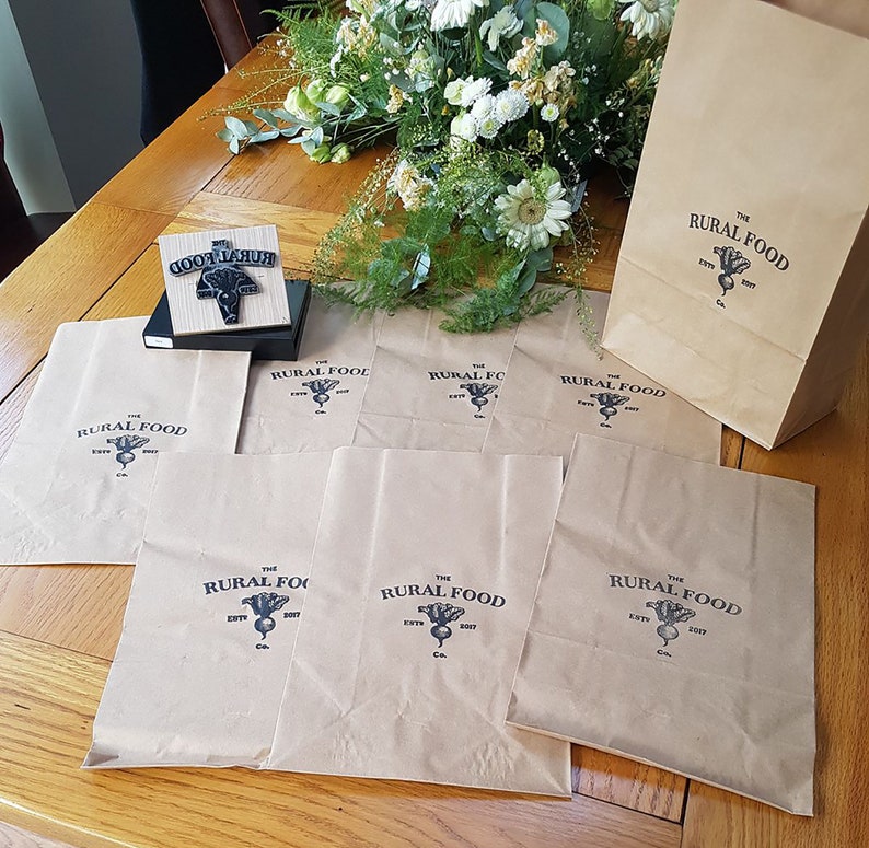 K&ouml;nnte beinhalten: Sieben braune Papiert&uuml;ten mit dem Logo "The Rural Food Co. Est. 2017" bedruckt. Das Logo zeigt eine Schwarzwei&szlig;illustration einer R&uuml;be.
