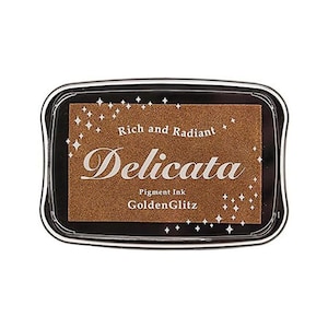 May include: A black and gold ink pad with the text "Rich and Radiant Delicata Pigment Ink GoldenGlitz" on the front.
