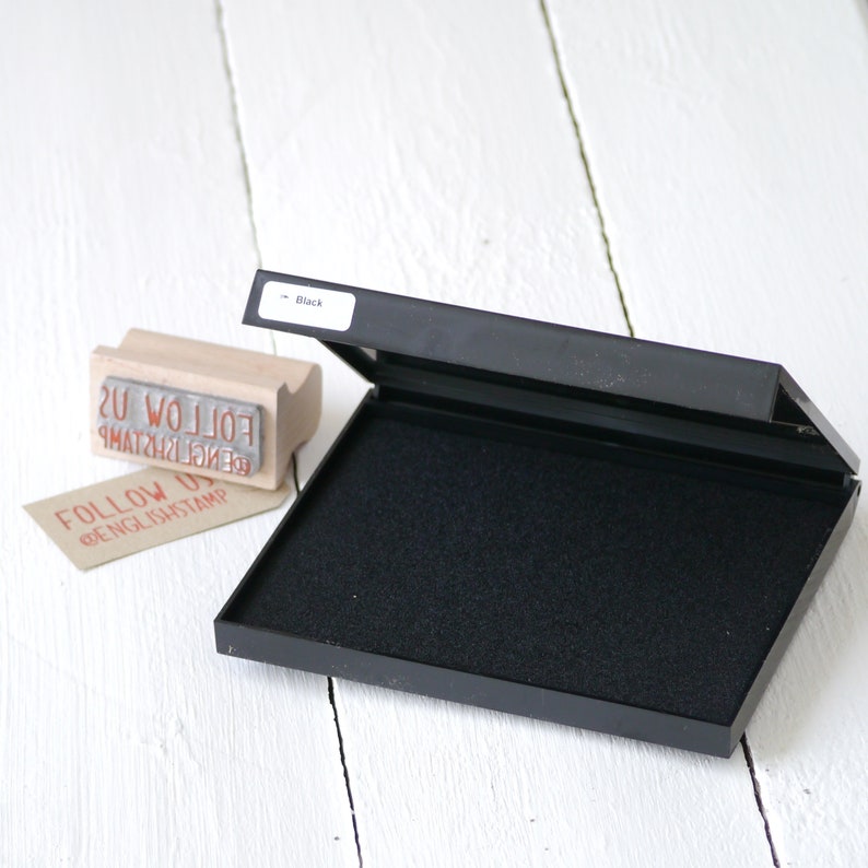 May include: Black ink pad with a black foam pad inside. The ink pad is open and the foam pad is visible. The ink pad is labeled "Black".