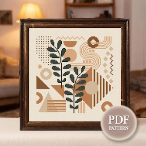 May include: Framed cross-stitch pattern featuring an abstract design with geometric shapes, including triangles, circles, and lines in shades of brown, beige, and black. Two dark green leafy branches are also included. The text "PDF PATTERN" is in the lower right corner.