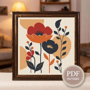May include: A framed cross-stitch pattern featuring stylized flowers in shades of red, orange, and navy blue, with tan and orange geometric shapes on a cream background. The frame is dark brown. The image includes a PDF pattern.