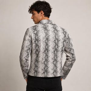 Peut inclure: Une veste &agrave; manches longues arborant un motif peau de serpent monochrome dans des tons de gris, noir et blanc. La veste pr&eacute;sente un col structur&eacute;, une fermeture boutonn&eacute;e sur le devant et une coupe ajust&eacute;e, port&eacute;e sur un pantalon noir.