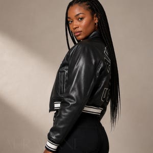 May include: Black cropped leather jacket with white striped trim on the cuffs and hem. The jacket has a classic bomber style with a small pocket on the chest and white lettering on the back that reads "USA".