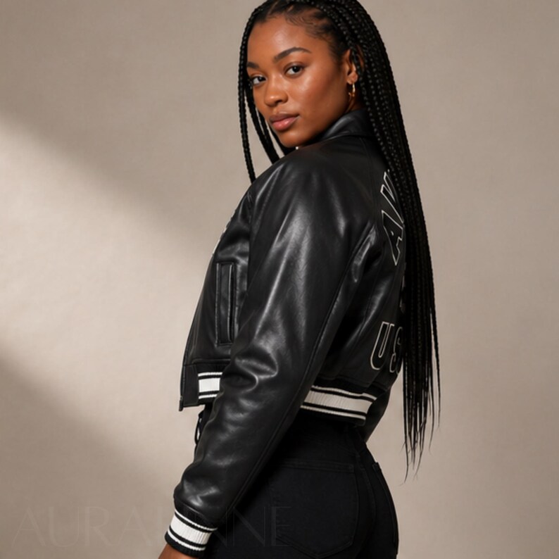 May include: Black cropped leather jacket with white striped trim on the cuffs and hem. The jacket has a classic bomber style with a small pocket on the chest and white lettering on the back that reads "USA".