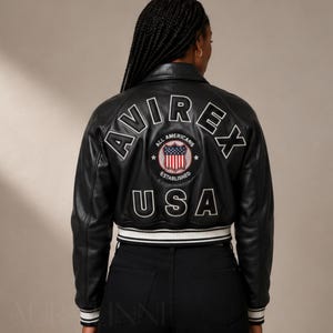 May include: Black leather bomber jacket with white trim and the word "AVIREX" in white lettering on the back. The jacket features a patch with the words "ALL AMERICANS ESTABLISHED USA".