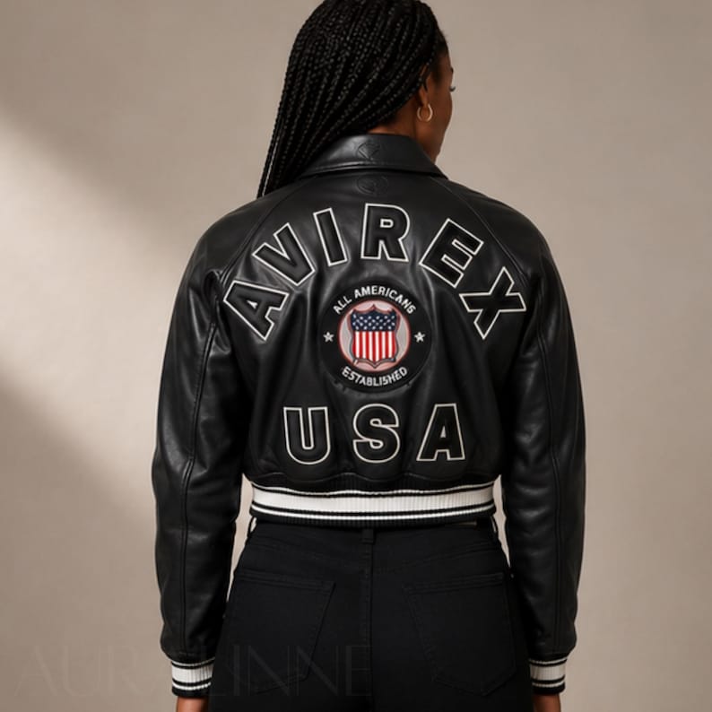 May include: Black leather bomber jacket with white trim and the word "AVIREX" in white lettering on the back. The jacket features a patch with the words "ALL AMERICANS ESTABLISHED USA".