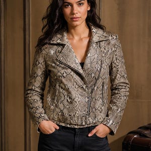 Puede incluir: Una chaqueta estilo motero con estampado de piel de serpiente en tonos beige, marrón y negro. La chaqueta incluye solapas con muescas, cierre de cremallera frontal asimétrico, mangas largas y un cinturón con hebilla en la cintura con herrajes plateados.
