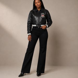 May include: A black leather jacket with a white and black striped trim on the cuffs and waist. The jacket has a patch on the chest. The model is wearing black flared jeans and black pointed-toe heels.