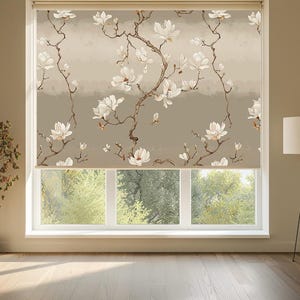 Könnte beinhalten: Ein Rollo mit beigem Hintergrund und einem sich wiederholenden Muster aus weißen Magnolienblüten und braunen Zweigen. Das Design umfasst weiche horizontale Streifen in verschiedenen neutralen Tönen und bedeckt das Fenster.