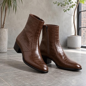 May include: A pair of brown ankle boots featuring a textured crocodile-embossed pattern. These boots have a pointed toe, a block heel, and a vertical zip closure on the inner side of the shaft. The finish is smooth with a subtle sheen.