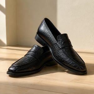 May include: A pair of black loafers featuring a textured crocodile-embossed pattern. The shoes have a classic slip-on design with a horizontal strap across the vamp, a rounded toe, and a low block heel, showcasing a polished finish throughout.