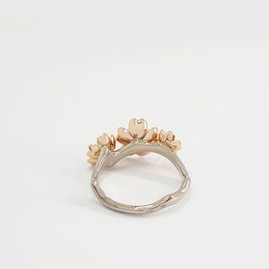 May include: A gold ring with three delicate flower designs. The ring is made of two-toned metal, with a white gold band and rose gold flowers.