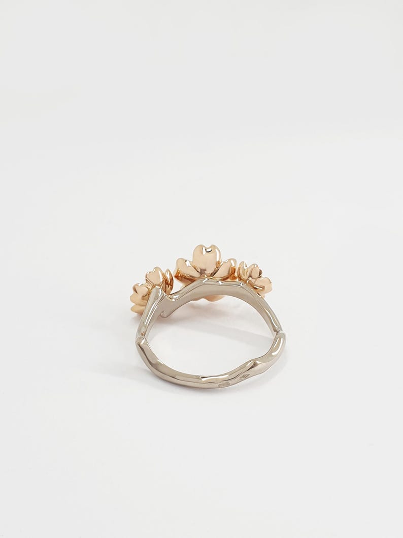 May include: A gold ring with three delicate flower designs. The ring is made of two-toned metal, with a white gold band and rose gold flowers.