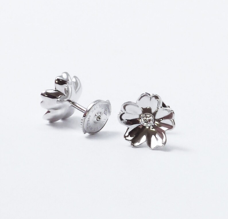 May include: A pair of silver flower-shaped earrings with a small diamond in the center of each flower.
