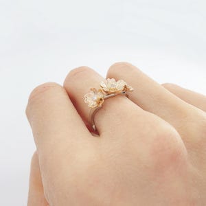 May include: A gold ring with three delicate flower designs, each with a small diamond in the center.