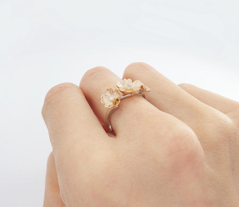 May include: A gold ring with three delicate flower designs, each with a small diamond in the center.