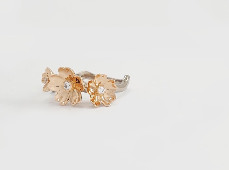 May include: A gold ring with three flower-shaped accents, each with a small clear stone in the center.