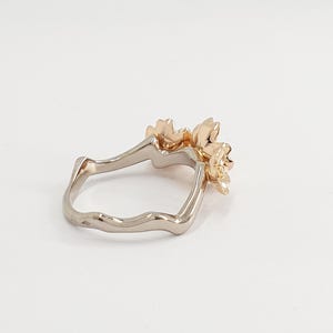 May include: A gold ring with a delicate floral design. The ring is made of two different metals, with a white metal band and a gold floral accent.