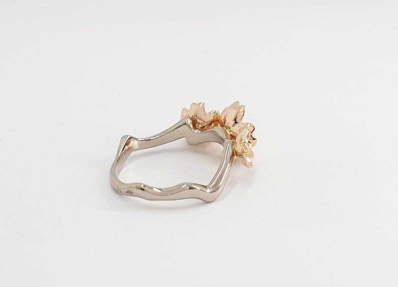 May include: A gold ring with a delicate floral design. The ring is made of two different metals, with a white metal band and a gold floral accent.