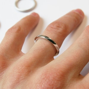 May include: A silver band ring worn on a person's finger.