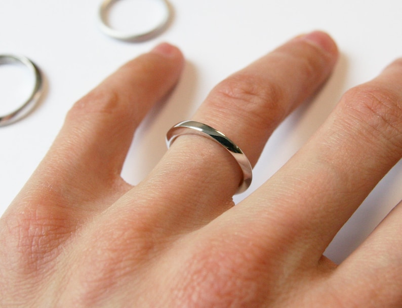 May include: A silver band ring worn on a person's finger.