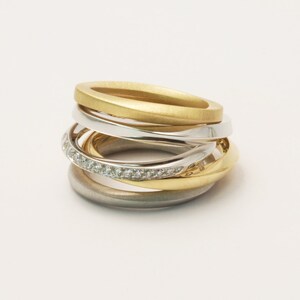 May include: A multi-band ring with a gold, silver, and white gold finish. The ring features a band of small diamonds.