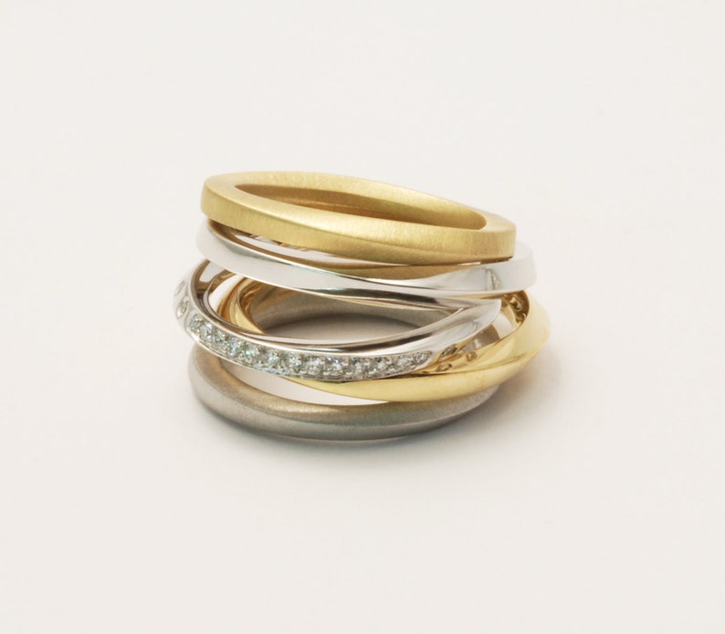May include: A multi-band ring with a gold, silver, and white gold finish. The ring features a band of small diamonds.